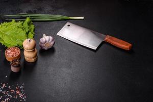 An axe for meat, spices and herbs, a cutting board against a dark concrete background photo