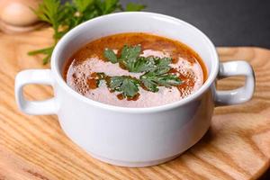 deliciosa sopa de tomate fresca con especias y perejil en un tazón blanco sobre una tabla de madera foto