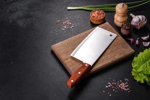 An axe for meat, spices and herbs, a cutting board against a dark concrete background photo