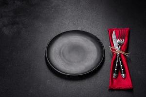 Christmas table setting with empty black ceramic plate, fir tree and black accessories photo