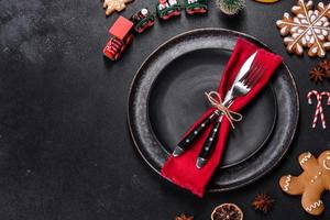 Christmas table setting with empty black ceramic plate, fir tree and black accessories photo