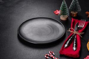 Christmas table setting with empty black ceramic plate, fir tree and black accessories photo