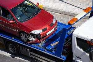 Crashed car loaded on a tow truck. Damage vehicle after crash accident on city street photo