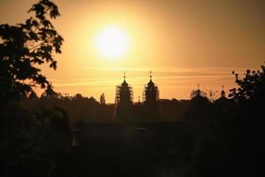 Kotryna's church with scaffolding for reconstruction silhouette in Vilnius orange and black sunset sky with tree branches and other buildings visible photo