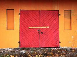 Bright red old wooden garage door double entrance door in orange wall building locked and nailed by a wooden plank photo