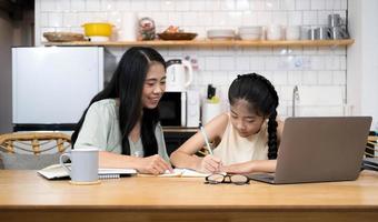 madre y niña asiática aprendiendo en una computadora portátil haciendo deberes estudiando conocimientos con el sistema de aprendizaje electrónico de educación en línea. videoconferencia infantil con profesor tutor en casa foto