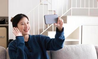 retrato hermosa joven asiática usa un teléfono móvil inteligente en el sofá en el interior de la sala de estar foto