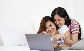un par de mujeres encantadoras escuchando canciones y viendo películas con una laptop en la cama mientras sonríen. son la felicidad y la construcción de buenas relaciones en el futuro. foto