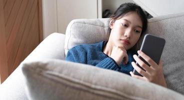 Asian lay on couch in living room frustrated with slow Internet connection or spam on smartphone. photo