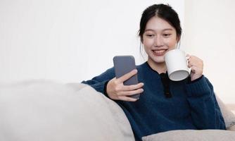 Close-up Of Smiling thailand Lady Having Cellphone Conversation And Enjoying Hot Drink While Relaxing On Couch. photo