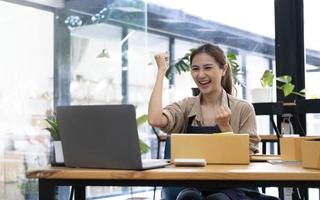 feliz joven empresaria asiática, sonríe por el éxito de las ventas después de revisar el pedido de la tienda de compras en línea en la oficina del hogar, concepto de negocio comercial en línea y comercio electrónico foto