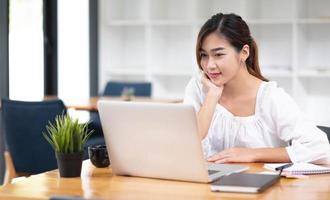 Happy young asian businesswoman sitting on her workplace in the office. Young woman working at laptop in the office. photo