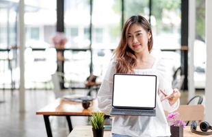 ropa de mujer asiática joven feliz sobre fondo blanco. concepto de estilo de vida de las personas. simulacro de espacio de copia. sostenga la computadora portátil con la pantalla vacía en blanco foto