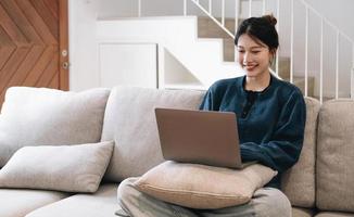 asian woman with laptop lying on comfy sofa and working remotely from home, mockup for website design. photo