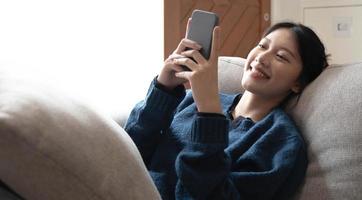 Portrait of smiling happy cheerful beautiful pretty asian woman relaxing making selfie photo on web camera.lying  on cozy sofa.