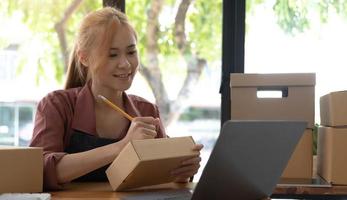 Retrato de mujer joven asiática SM trabajando con una caja en casa el lugar de trabajo.Propietario de una pequeña empresa de inicio, pequeña empresa emprendedora o empresa independiente en línea y concepto de entrega. foto