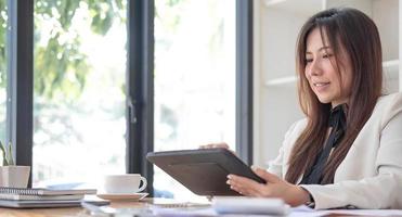 Beautiful young asian woman sitting at coffee shop using laptop. Happy young businesswoman sitting at table in cafe with tab top computer. photo