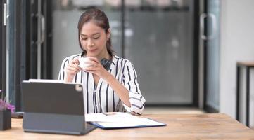 Image of a young woman smiling through a laptop's web camera while holding a cup of coffee in the kitchen at home. photo