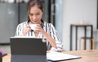 Image of a young woman smiling through a laptop's web camera while holding a cup of coffee in the kitchen at home. photo