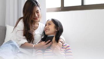 Young beautiful Asian women lesbian couple lover using smartphone video call online in living room on sofa at home with smiling face.Concept of LGBT sexuality with happy lifestyle together. photo