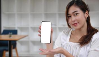 imagen de una maqueta de una hermosa mujer asiática sonriente sosteniendo y mostrando un teléfono móvil negro con pantalla blanca en blanco. foto