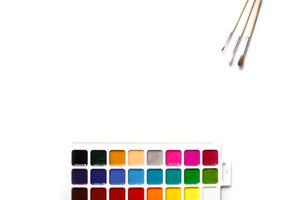 A palette of eighteen-color watercolors and paintbrushes on a white background with space for text. photo