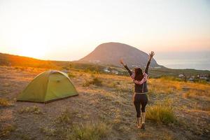 Woman meets the dawn in the mountains, rejoices in the sun. Panoramic view of the mountain and the sea from above. Camping, outdoor activities, sports mountain hiking, family travel. Ayu-Dag, Crimea. photo