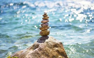 A pyramid of pebbles on a large stone against the background of the sea and the sun's glare on the water. Tour, tourism, vacation at the resort, swimming. Travel background, sunscreen. Copy space photo