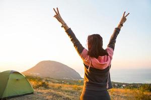 Woman meets the dawn in the mountains, rejoices in the sun. Panoramic view of the mountain and the sea from above. Camping, outdoor activities, sports mountain hiking, family travel. Ayu-Dag, Crimea. photo