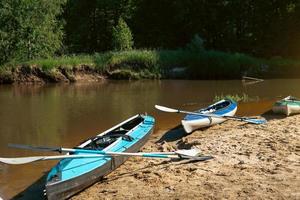 Tourist canoes with paddles stand on the river coast in summer on a water hike. Rafting on inflatable and frame double and triple kayak boats, family trip, extreme adventure in summer photo