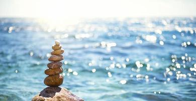 A pyramid of pebbles on a large stone against the background of the sea and the sun's glare on the water. Tour, tourism, vacation at the resort, swimming. Travel background, sunscreen. Copy space photo