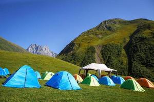 Tourist camping in the mountains of many tents and shelters for climbing to the top of the mountain - an alpine camp. Overnight in nature. Georgia, Chaukhi Mountain, Jute village photo