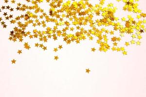 Gold sequins in the shape of stars shimmer on a pink background. Backgrounds with copyspace for a holiday, party decoration, Christmas and new year, birthday and anniversary. Gradient and texture photo