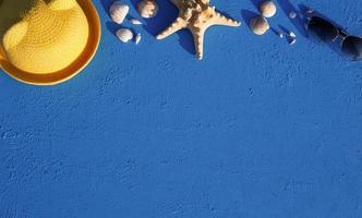 marco con accesorios de playa sobre un tema náutico sombrero de paja amarillo, gafas de sol, estrellas de mar y conchas sobre un fondo azul. concepto de vacaciones, viaje por mar, protección uv, natación. copie el espacio plano foto