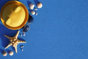 marco con accesorios de playa sobre un tema náutico sombrero de paja amarillo, gafas de sol, estrellas de mar y conchas sobre un fondo azul. concepto de vacaciones, viaje por mar, protección uv, natación. copie el espacio plano foto