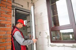 Master sets up a door handle with multi-lock plastic door with wood lamination and gold layout in private house. Installation of windows and doors, glazing of the cottage, replacement of the mechanism photo