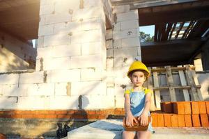 una niña pequeña con un casco amarillo está jugando al constructor en el sitio de construcción de su futuro hogar. expectativa de mudanza, elección de profesión, educación de los hijos. futura profesión, empresa familiar. foto