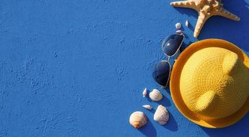 Frame with beach accessories on a nautical theme yellow straw hat, sunglasses, starfish and shells on a blue background. Vacation concept, sea trip, UV protection, swimming. Copy space. Flatlay photo