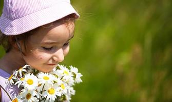 Little girl with a bouquet of daisies in summer on a natural background. Happy child,panama hat for sun protection. International Children's Day. Copy space. Authenticity, rural life, eco-friendly photo