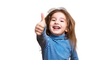 A little girl of Caucasian appearance in a blue striped turtleneck shows a thumbs up and laughs, smiling happily. White background, isolate.