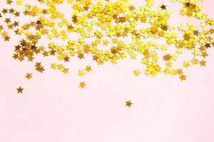 Gold sequins in the shape of stars shimmer on a pink background. Backgrounds with copyspace for a holiday, party decoration, Christmas and new year, birthday and anniversary. Gradient and texture photo