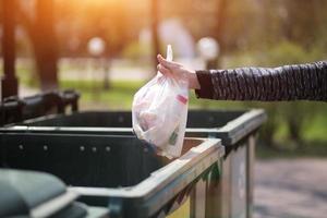 mano con una bolsa de basura plástica sobre contenedores para separación y clasificación en rusia con las palabras vidrio, plástico, desechos domésticos. foto