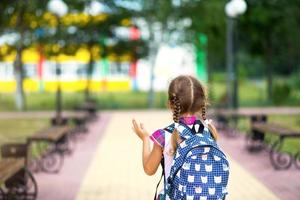 Cheerful girl with a backpack and in a school uniform in the school yard back to the frame. Back to school, September 1. A happy pupil. Primary education, elementary class. Road to life, to knowledge photo