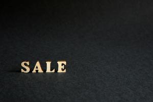 inscription Sale of wooden letters on a black background. Black Friday, discounts, sale, shopping, interest sign. Space for text photo