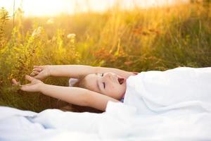 Girl sleeps on bed in grass, Sweet stretches and yawns sleepily, good morning in fresh air. Eco-friendly, healthy sleep, benefits of ventilation, hardening, clean nature, ecology, children's health photo