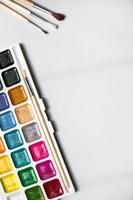 A palette of eighteen-color watercolors and paintbrushes on a white background with space for text. photo