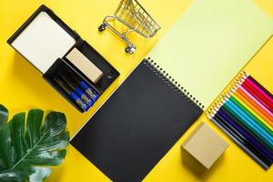 Layout of multi-colored stationery on a yellow background spiral notebook, colored pencils, stand, pens, indoor flower. Business flat lay, mock up. Sheets for notes, office work. Back to school photo