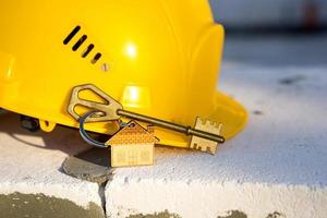 Construction yellow hardhat and key to house on window of housing made of blocks of porous concrete. Turnkey construction, future home, engineering, building. Work safety. Copy space photo