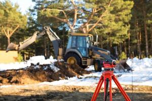 A geodesic level stands in front of a bulldozer for excavating a pit at a construction site. The excavator bucket digs a hole for building a house in the countryside. photo