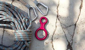 Coiled climbing rope and steel carabiner. Mountain climbing equipment harness, brakes, quickdraws, self-insurance, belay device eight. On a stone background with cracks. Flatlay, copy space photo